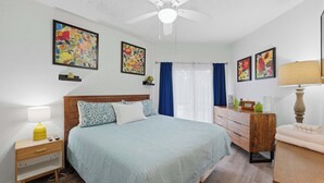 A bedroom with a bed, bedside tables, a dresser, a ceiling fan, and floral artwork on the walls. - Treetops at Inverness (New Braunfels)