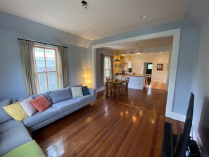 Ein Wohnzimmer mit einer Couch, Holzboden und einer Küche im Hintergrund.