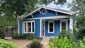 A blue house with a front porch, a small garden with various plants, and a gravel pathway leading to the door. - Gorgeous Zilker Cottage - Monthly Rental - Available August (Austin)