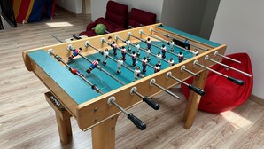 Una mesa de fútbol en una habitación con piso de madera, un sillón de peluche rojo y una silla roja.