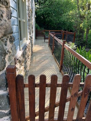 A wooden deck with a metal railing, leading to a stone building with a window.