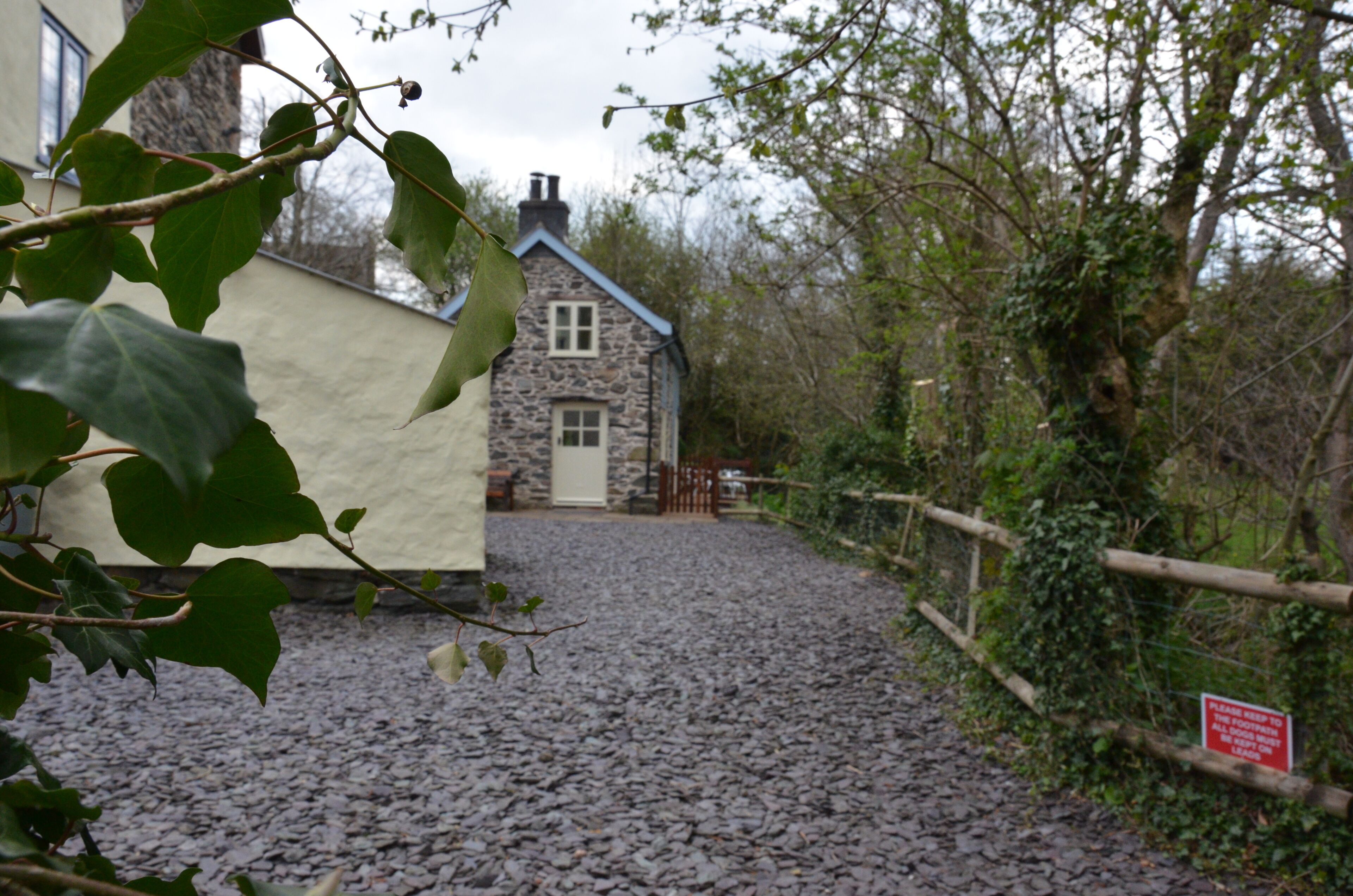 A stone cottage with a gravel driveway leading to a wooden gate.