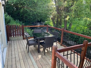 Eine Holzterrasse mit Tisch und Stühlen, umgeben von einem Metallgeländer und Grünpflanzen.