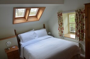A bedroom with a single bed, a nightstand, a bedside table, a window with floral curtains, and a skylight.