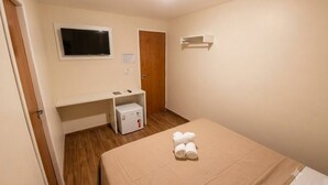 Una habitación de hotel con cama, televisión, escritorio pequeño, calefactor y puerta.