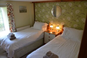 A twin room with two beds, a nightstand with lamps, a window with curtains, and a floral wallpaper. - Hafannedd stunning Mill, with Gardens and River Views (Corwen)