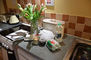 A kitchen counter with a toaster, a vase with flowers, a bread container, a milk carton, a jar, and a bag of bread. - Hafannedd stunning Mill, with Gardens and River Views (Corwen)