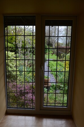 A room with a view through a window with a grid pattern, leading to a garden with various plants and a bench. - Hafannedd stunning Mill, with Gardens and River Views (Corwen)