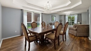 Een eetkamer met een grote houten tafel, stoelen en kroonluchters.