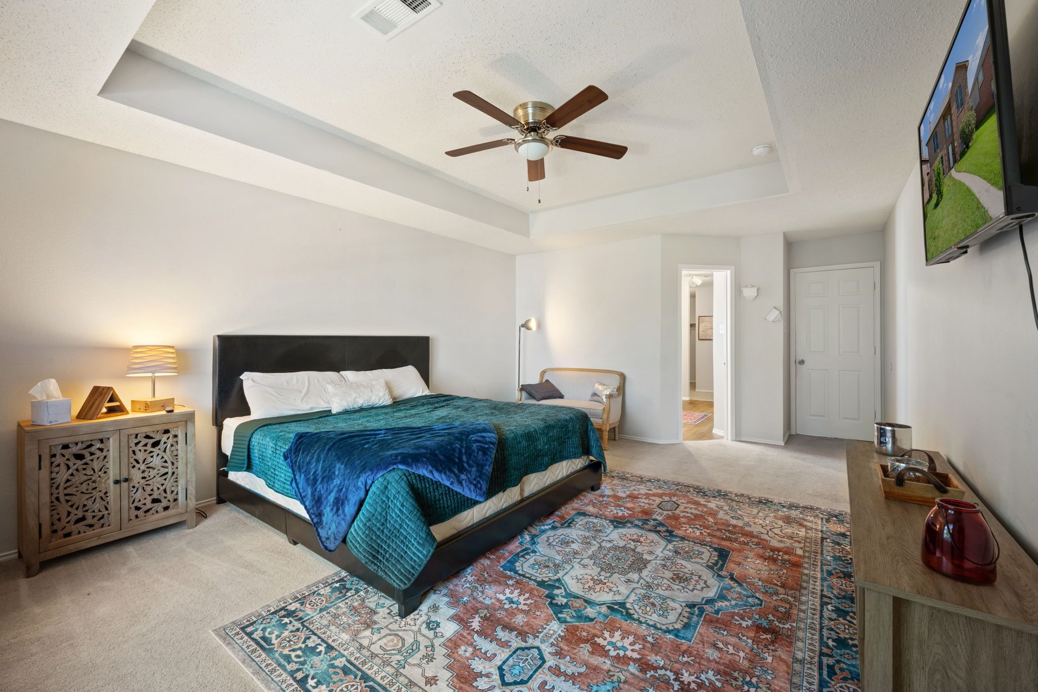 A bedroom with a bed, a ceiling fan, a TV, a nightstand, and a rug.