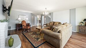 Een woonkamer met een bank, een salontafel, een stoel, een open haard en een kroonluchter.