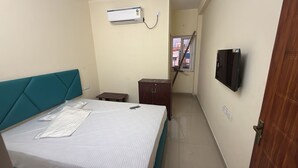 Une chambre à coucher comprenant un lit, une petite table, une armoire, un appareil de climatisation, un téléviseur et une fenêtre.