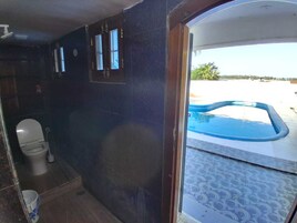 Casa de banho com sanita, uma pequena janela e vista para uma piscina exterior.
