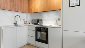 Una cocina moderna con armarios blancos, horno empotrado, microondas y alacenas de madera.