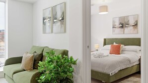 Una habitación con un sofá verde, una cama con cabecera verde y dos cuadros abstractos en la pared.