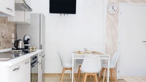 A modern kitchen with white cabinetry, a built-in oven, and a coffee machine. There is a dining table with four chairs and a clock on the wall. - La Dimora di Vanna by Rentbeat (Avola)