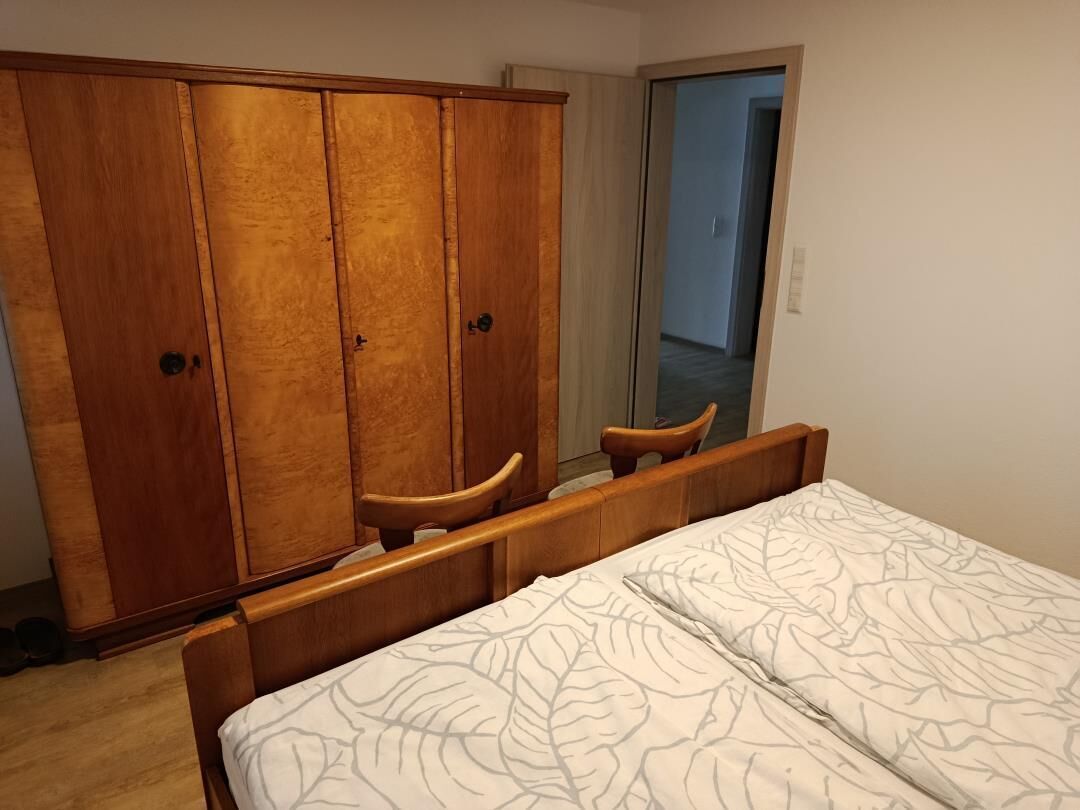 A bedroom with a bed, wooden wardrobe, and a mirror.