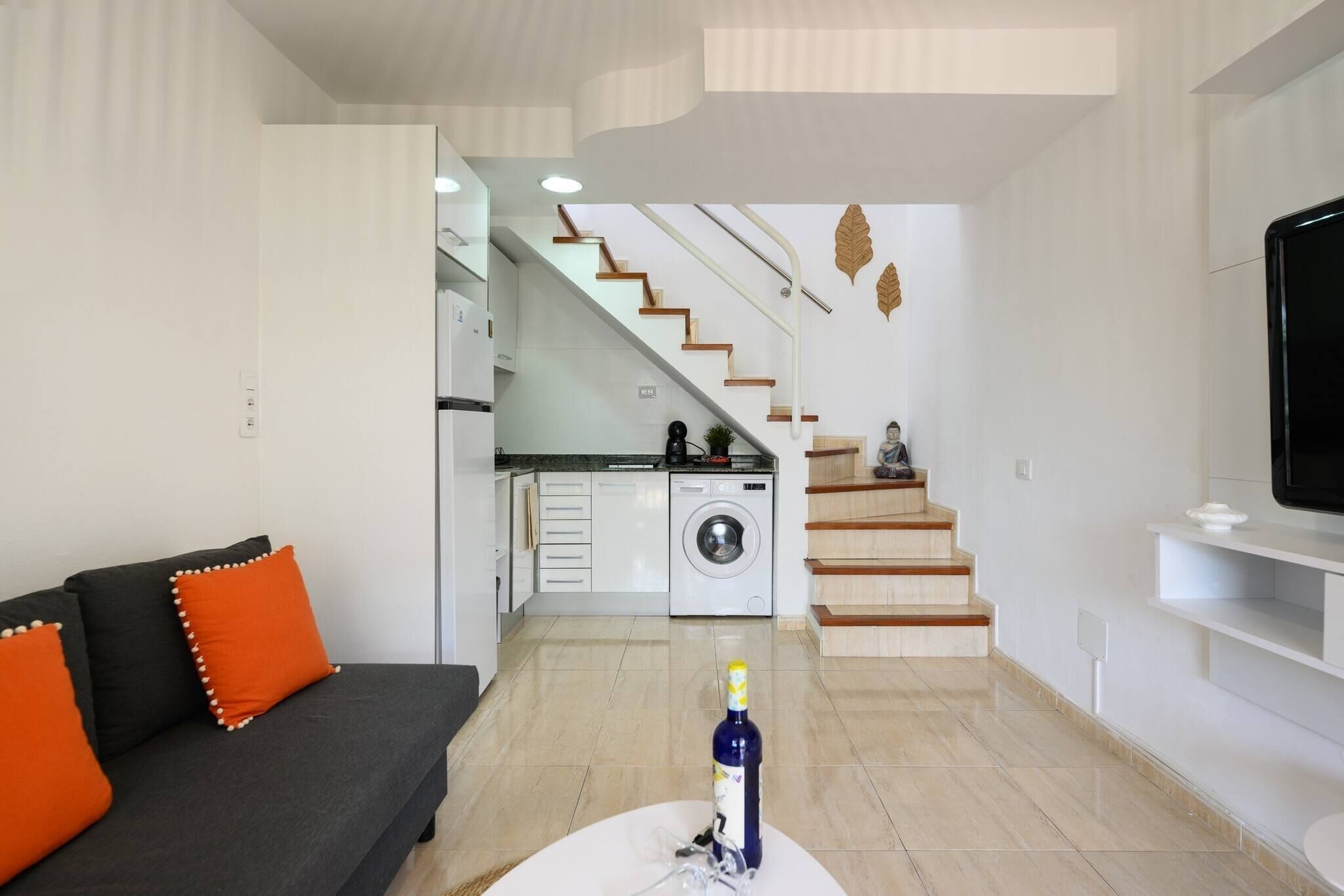 Una sala de estar moderna con sofá, mesa de centro, televisor, escalera y lavadora.