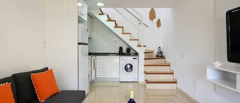Una sala de estar moderna con sofá, mesa de centro, televisor, escalera y lavadora.