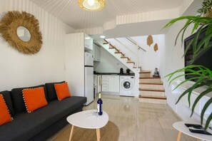 A modern living room with a sofa, a small table, a kitchen in the background, and a staircase leading to another level. - Beverly Hills Bungalow (San Bartolomé de Tirajana)