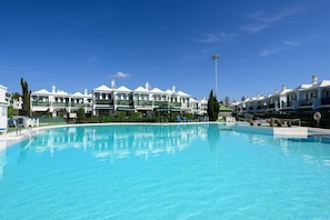 A swimming pool with lounge chairs and a row of white buildings with green accents. - Beverly Hills Bungalow (San Bartolomé de Tirajana)