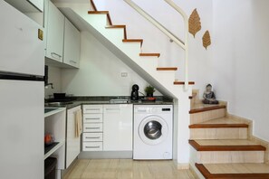 Een compacte keuken met een ingebouwde wasmachine, houten trap en een klein beeldje.