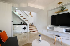 Een moderne woonkamer met een flatscreen televisie, een bank, een salontafel en een trap die naar een keuken leidt.