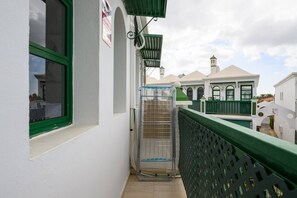 A balcony with a metal rack, a window with green trim, and a building with a white facade and green accents in the background. - Beverly Hills Bungalow (San Bartolomé de Tirajana)
