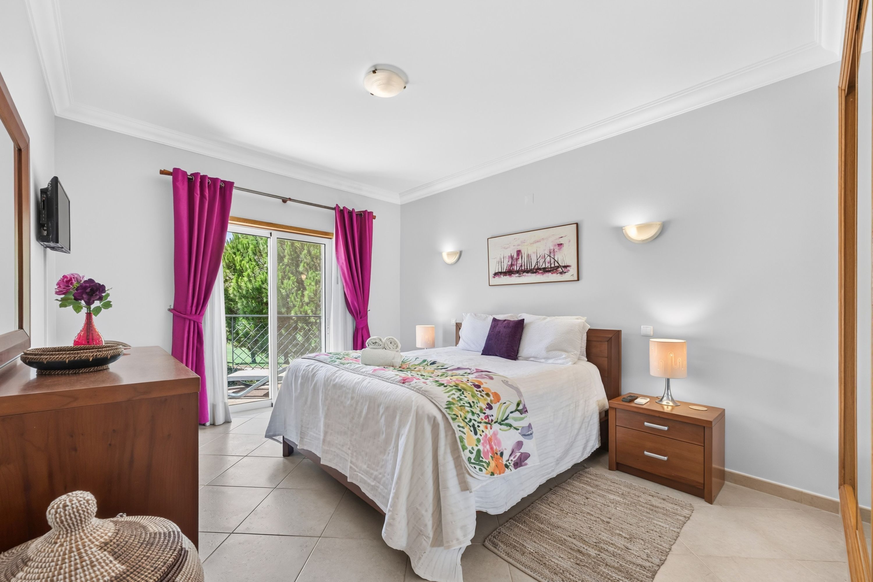 Ein Schlafzimmer mit einem Bett, Nachttischen, einem Schreibtisch, einem Stuhl, einem Fenster mit Vorhängen und einer Tür.