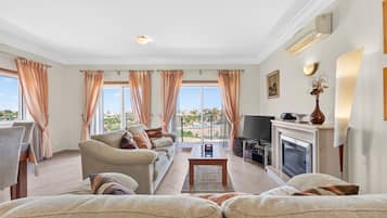 Una sala de estar con sofá, sillones, chimenea, televisor y un balcón con cortinas.