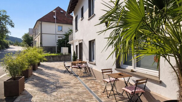 Un patio con mobiliario exterior, una planta en maceta y un edificio con techo de tejas.