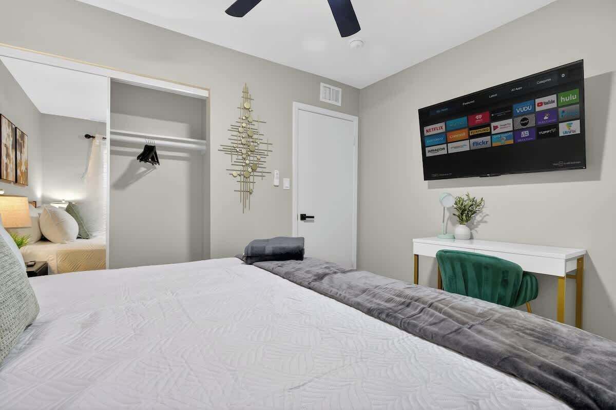 A bedroom with a bed, a desk, a TV displaying streaming services, and a decorative wall piece.