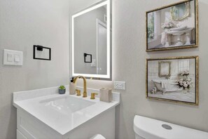 Een badkamer met een groot wit wastafelblad, een gouden kraan, een spiegel en twee lijstjes met foto's aan de muur.