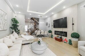 Ein modernes Wohnzimmer mit Sofa, Couchtisch, Fernseher und einer Treppe, die in einen Essbereich führt.