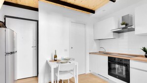 Una cocina moderna con armarios blancos, encimera de madera, horno empotrado y zona de comedor con mesa y sillas blancas.