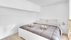 Un dormitorio minimalista con cama, paredes blancas y suelo de madera.