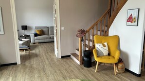 A living room with a sofa, a yellow armchair, a staircase, and a painting on the wall. - Le Clos des Pères House: 120 m², 3 bedrooms, 2 bathrooms, fenced-in yard. Pets allowed (Monflanquin)