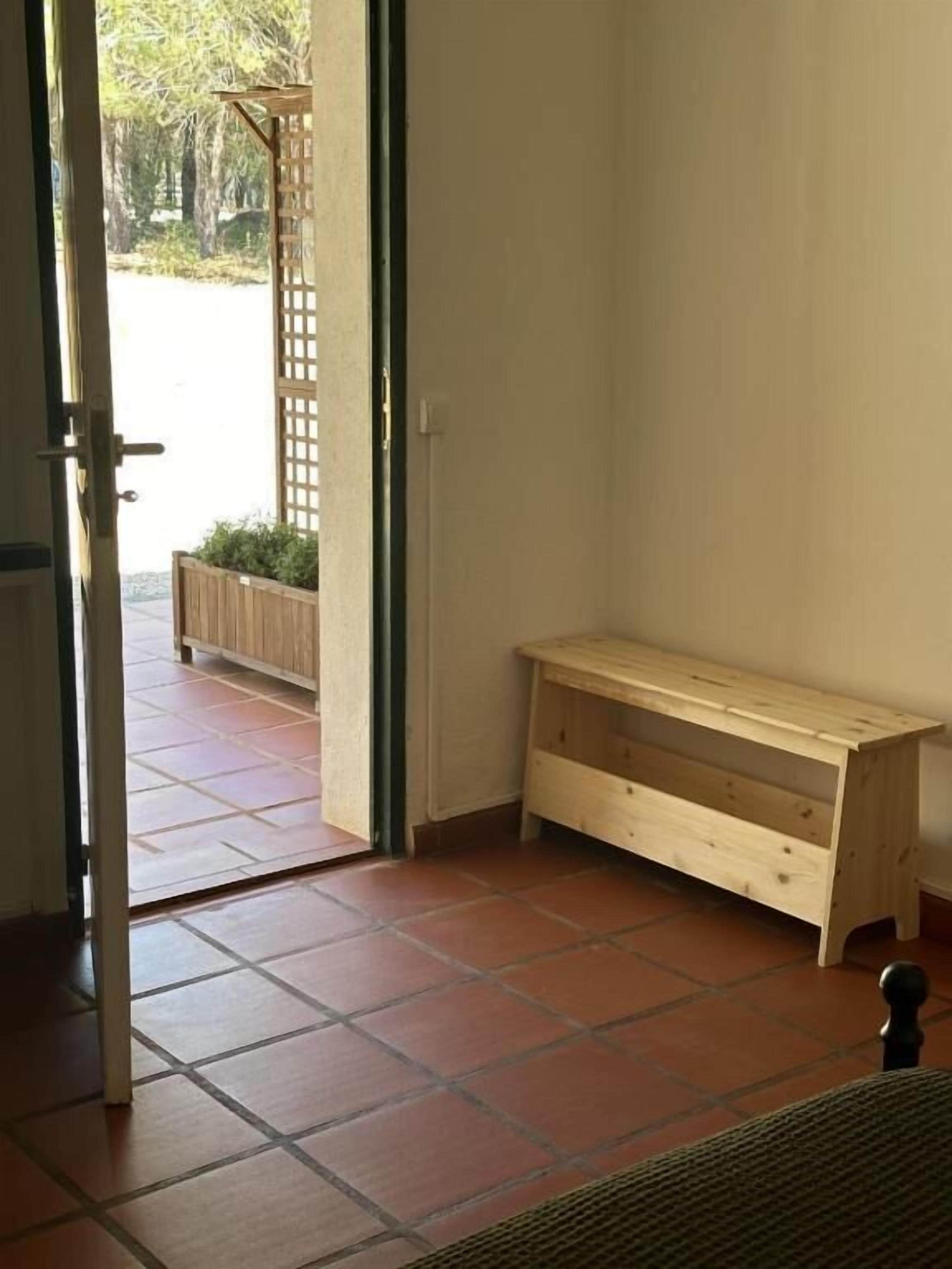Una habitación con un banco de madera, una puerta que da al exterior y piso de baldosas.