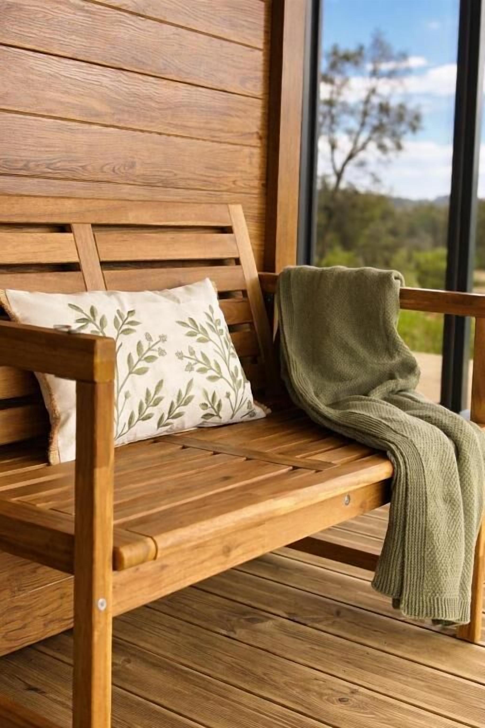 A wooden bench with a cushion and a blanket.