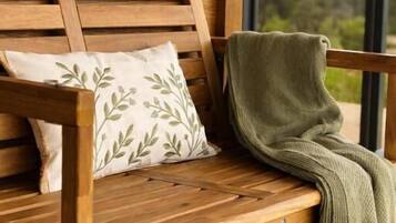 A wooden bench with a cushion and a blanket.