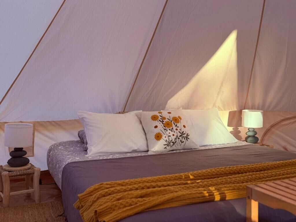 A tent with a bed, pillows, a lamp, and a blanket.