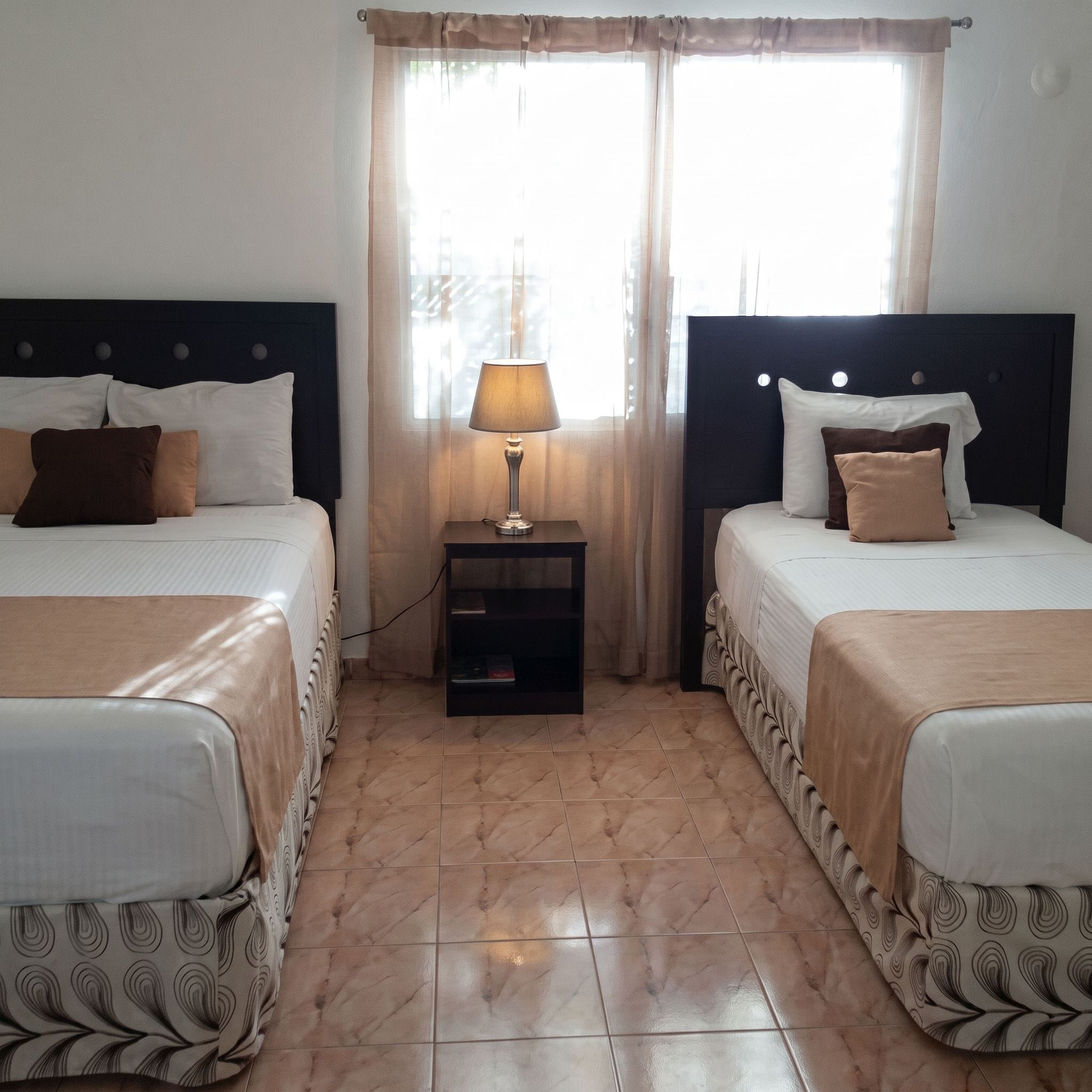 Une chambre d’hôtel avec deux lits, une table de chevet avec une lampe et une fenêtre avec des rideaux.