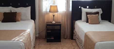 Habitación de hotel con dos camas, una mesita de noche con lámpara y un ventanal con cortinas.