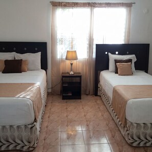 Habitación de hotel con dos camas, una mesita de noche con lámpara y un ventanal con cortinas.