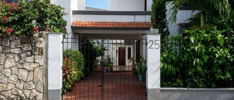 A gated entrance to a building with a stone wall on the left, a metal gate, and a number '25' on the right.
