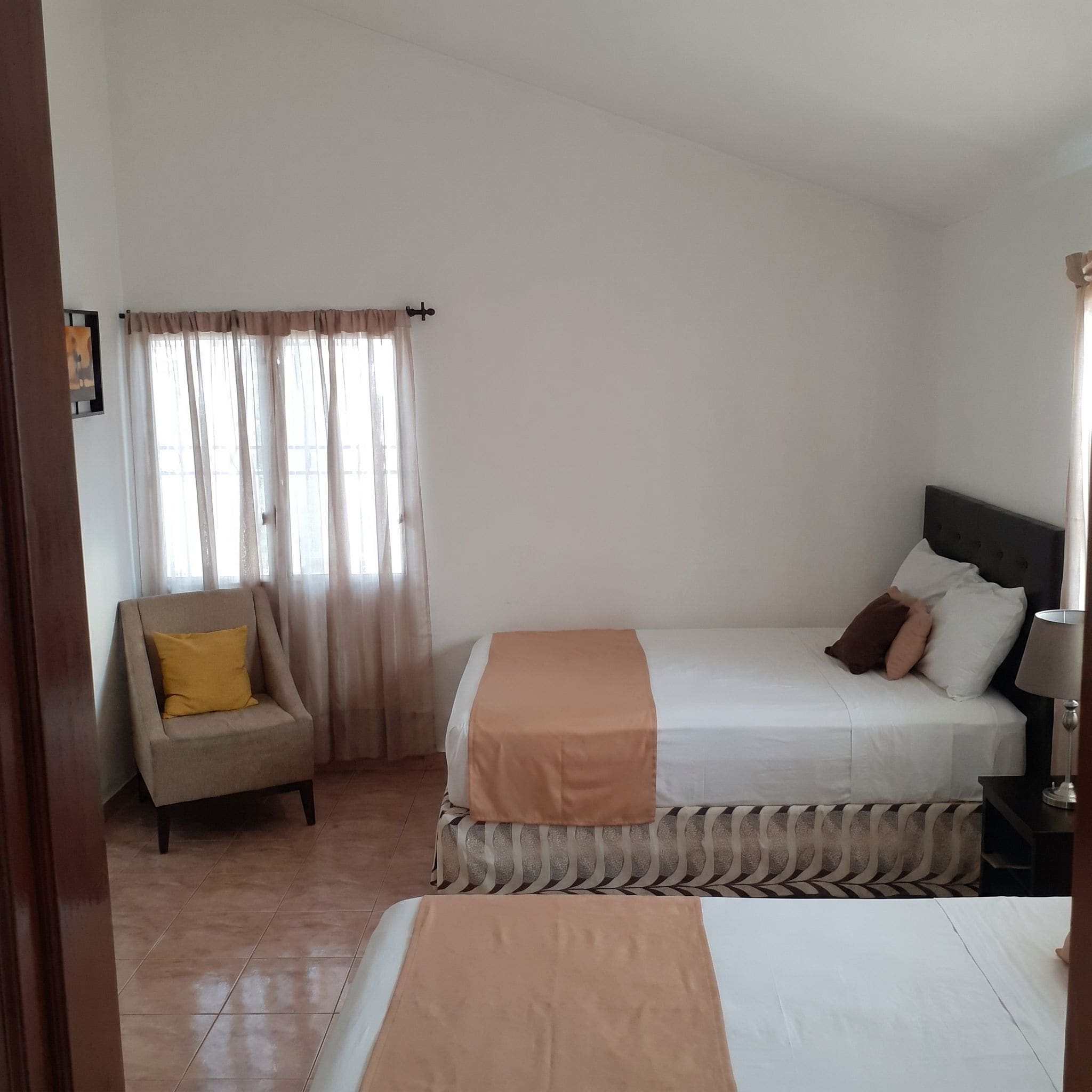 Une chambre d’hôtel avec un lit, une chaise, une table de chevet et une fenêtre avec des rideaux.