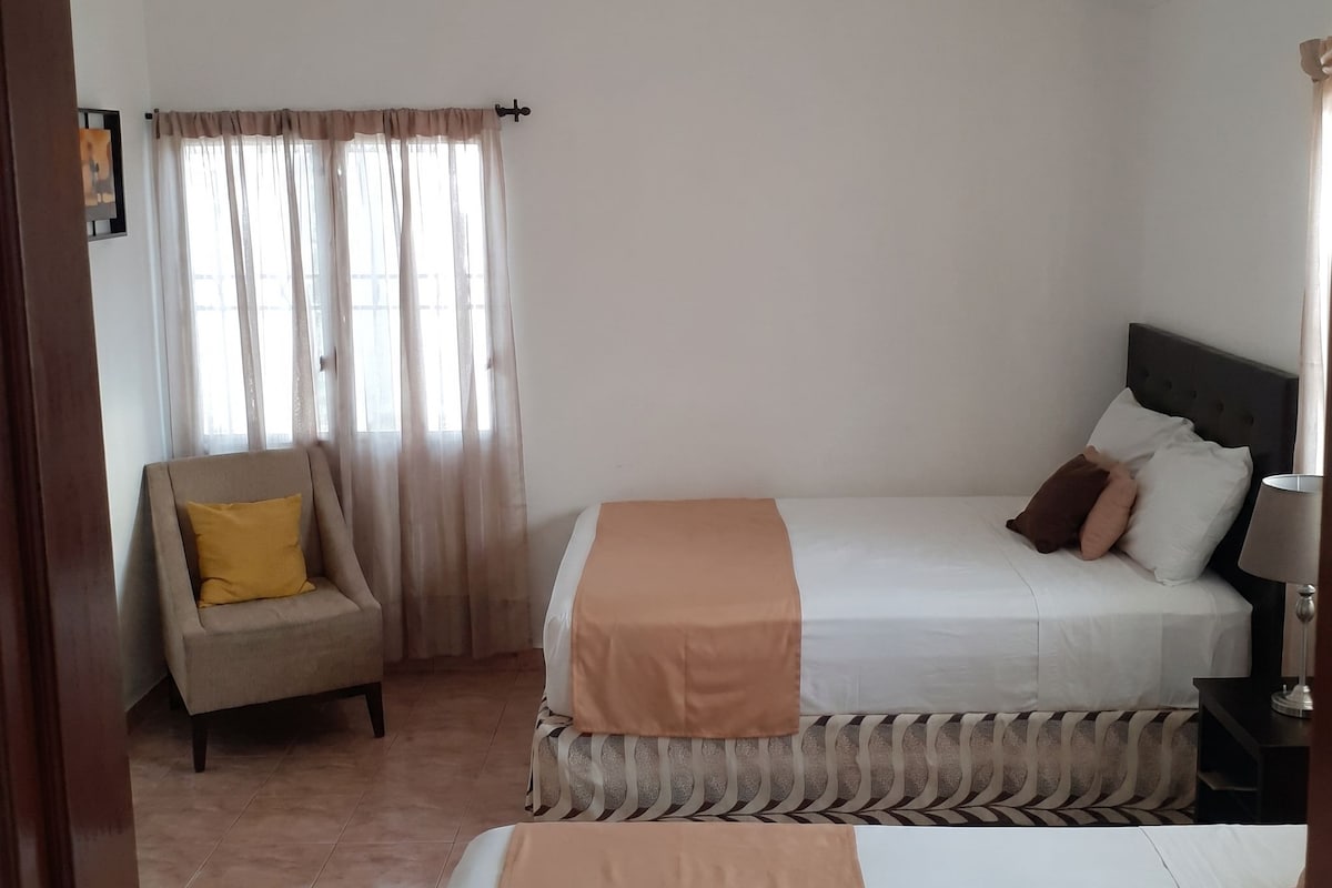 A hotel room with a bed, a chair, a nightstand, and a window with curtains.