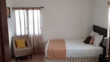 Une chambre d’hôtel avec un lit, une chaise, une table de chevet et une fenêtre avec des rideaux.