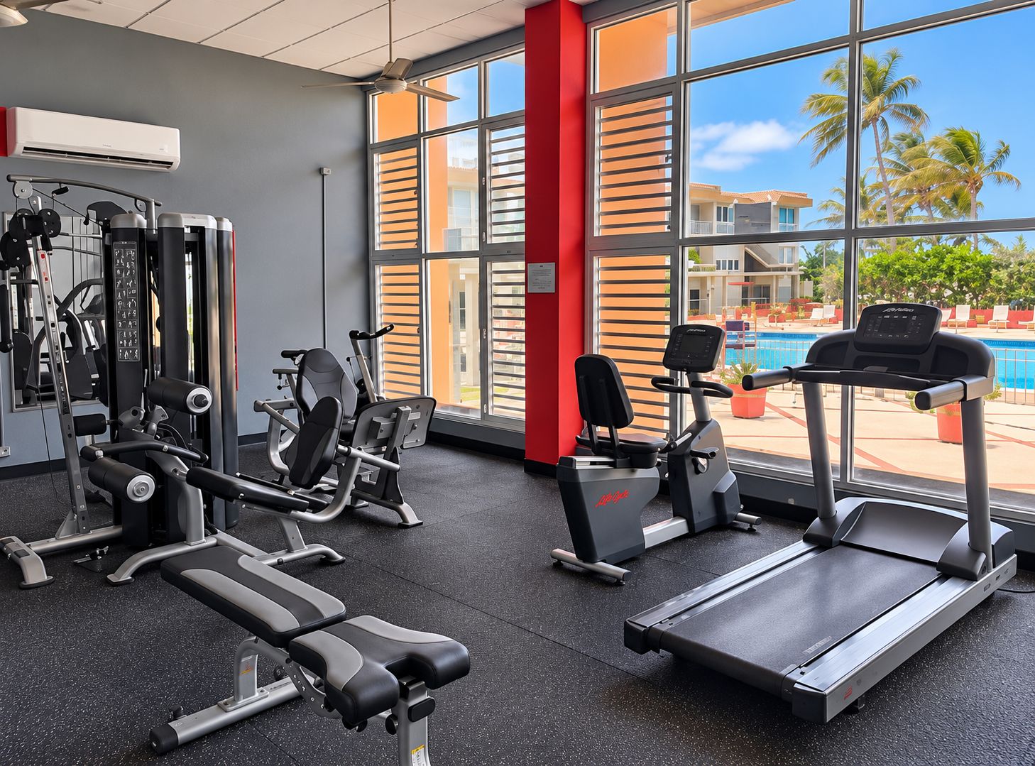 A gym with exercise equipment, large windows, and a view of a pool.