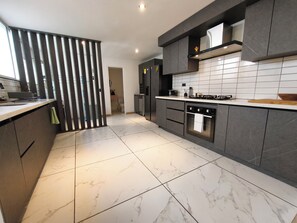 A modern kitchen with a marble floor, dark cabinetry, and a central island. - Bright 3BR Oasis • 500Mbps WiFi & 24/7 Security (Medellín)
